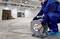 A man in workwear is winding a long cable onto a cable drum in a large, empty warehouse.