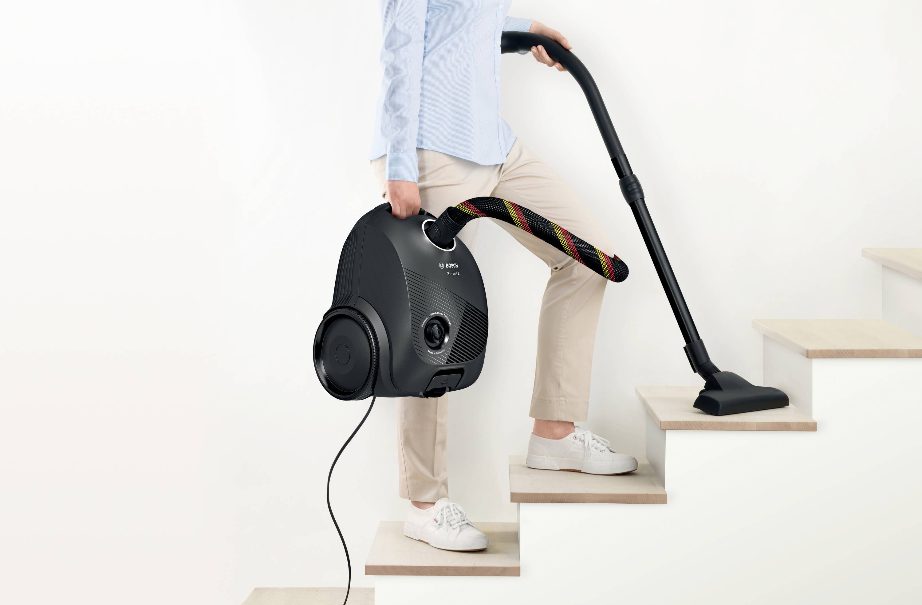 A person is climbing stairs with a vacuum cleaner that is marked with the text 'light'.