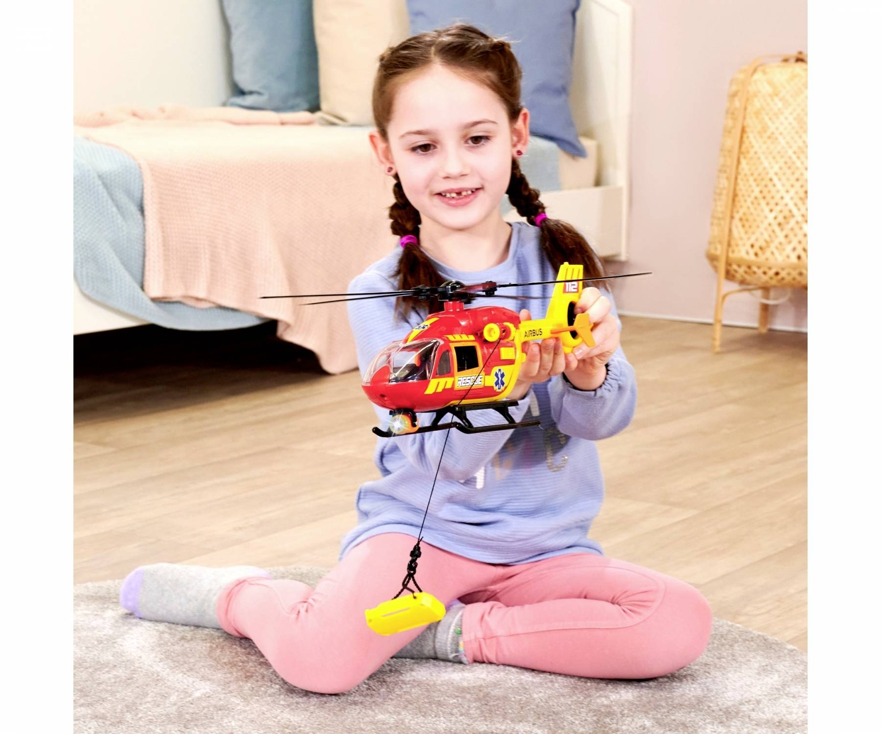 A child is sitting on the floor, playing with a model rescue helicopter. A bed is visible in the background.