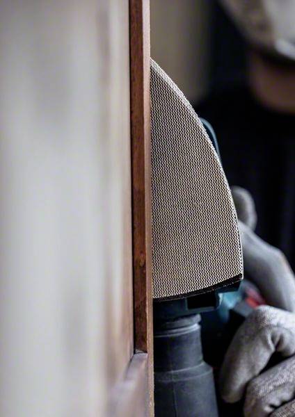 Close-up of a person using an electric sander to smooth wood. The person is wearing work gloves.