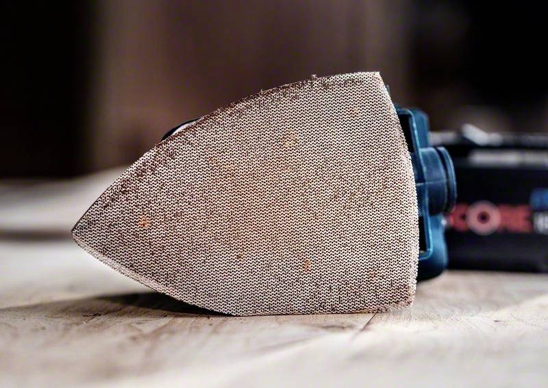A grinding machine with a triangular grinding head lies on a wooden table, ready for woodworking.
