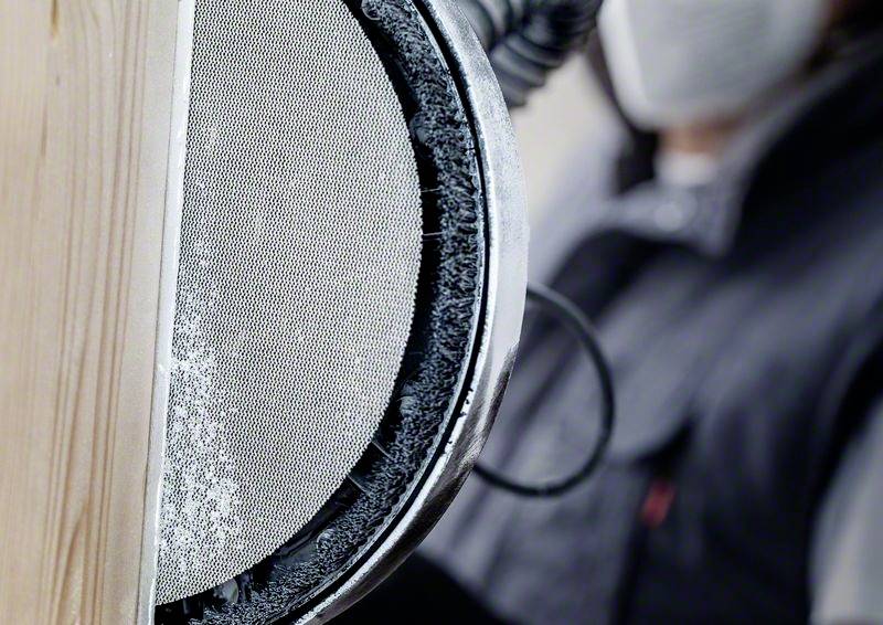 A person is sanding a wooden surface with an electric sanding tool. A dust mask is being worn for protection.