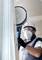 A construction worker wearing a hard hat and mask is grinding a wall with an electric sander inside a room.