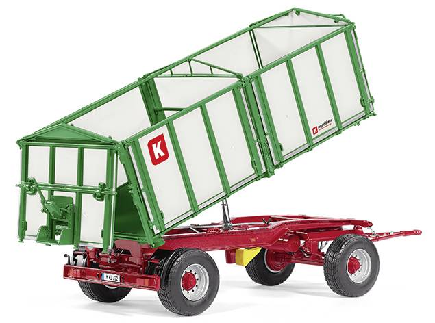 A green agricultural trailer with red wheels is tipping sideways. Brand logos are visible.