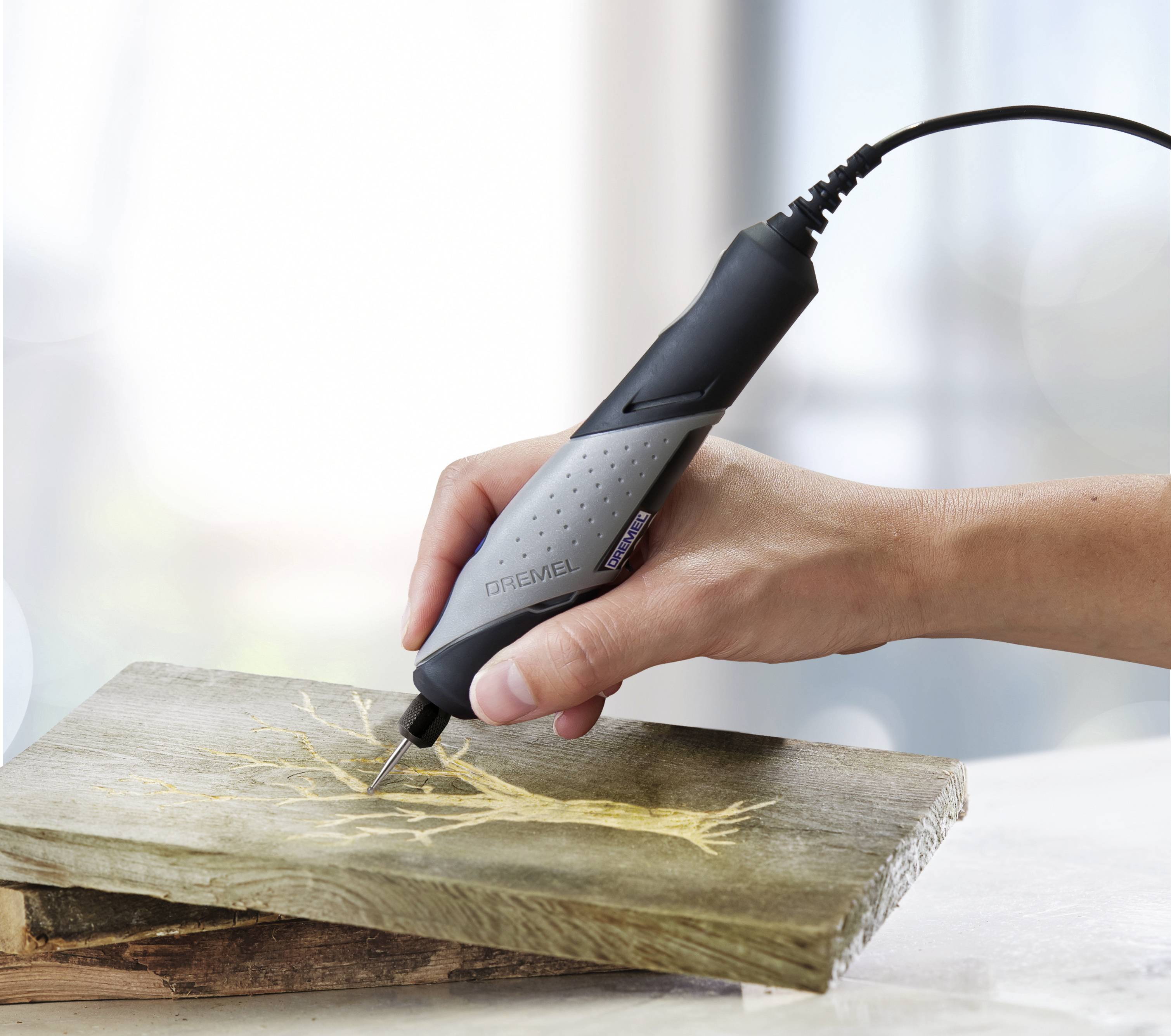 A hand is using a handy, electric tool to engrave a tree design into a wooden board.
