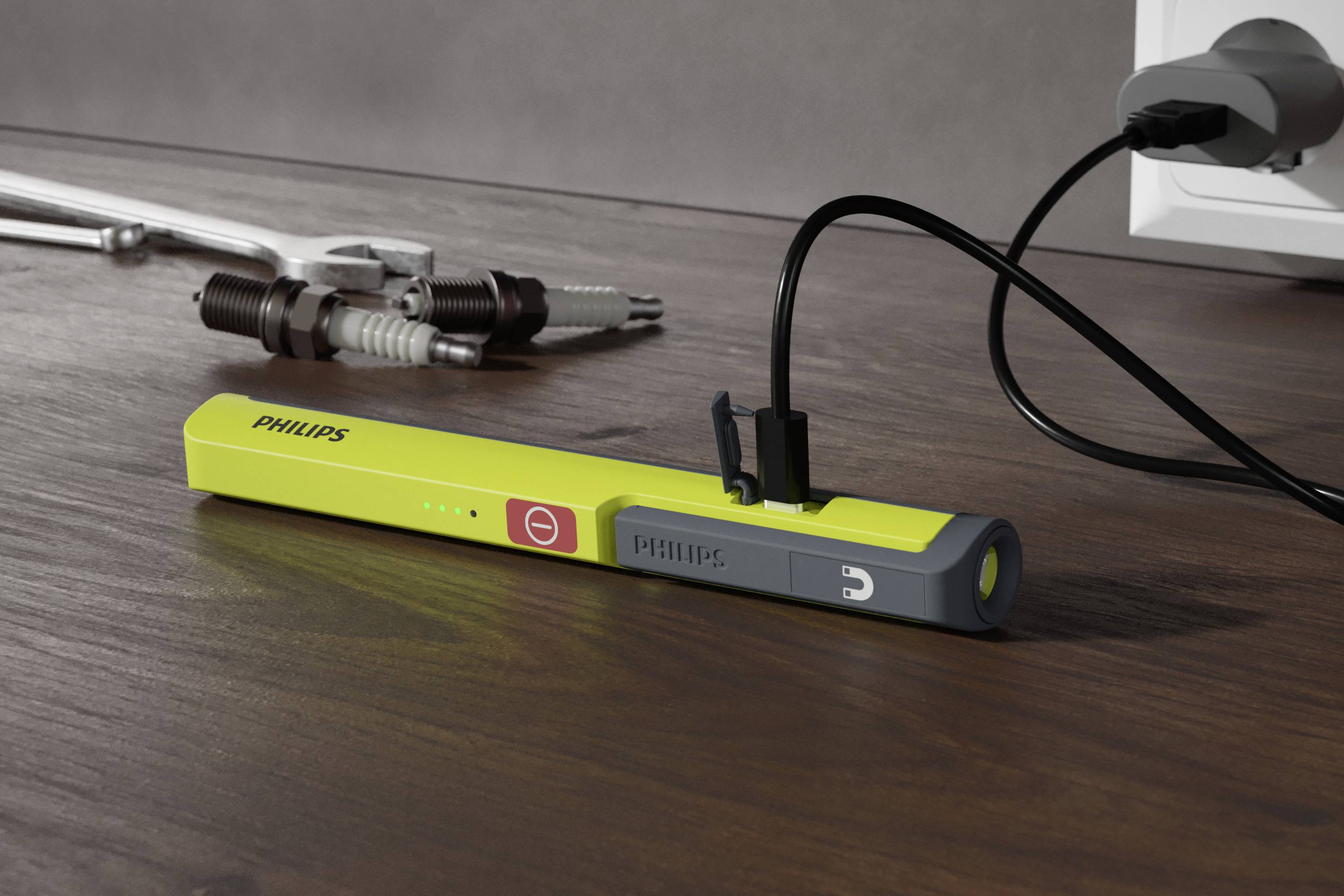 A yellow, rectangular Philips device lies on a wooden table. It is connected to a power source. Tools can be seen in the background.