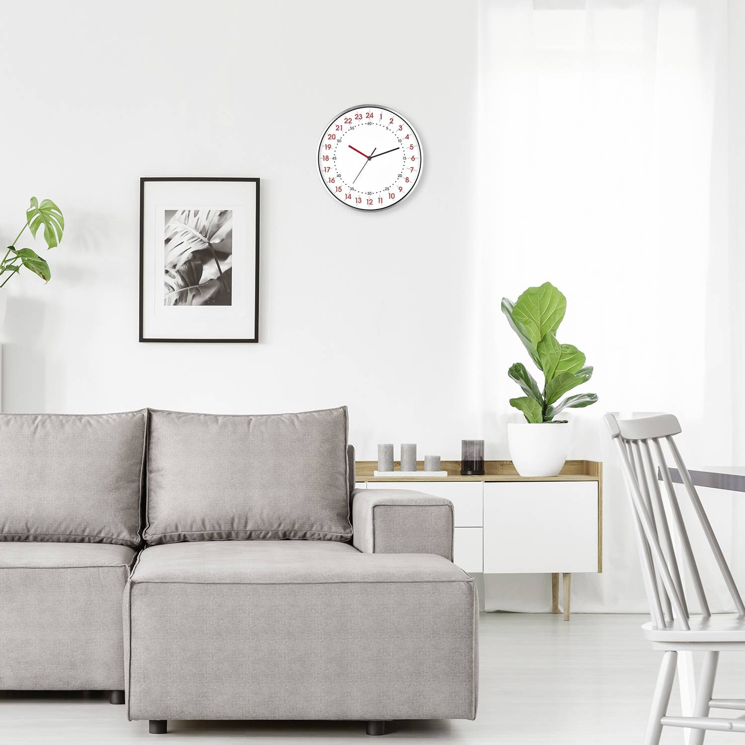 Bright living room with a grey sofa, wall clock showing 10:10, plants and artwork as decoration, creating a calm and modern atmosphere.