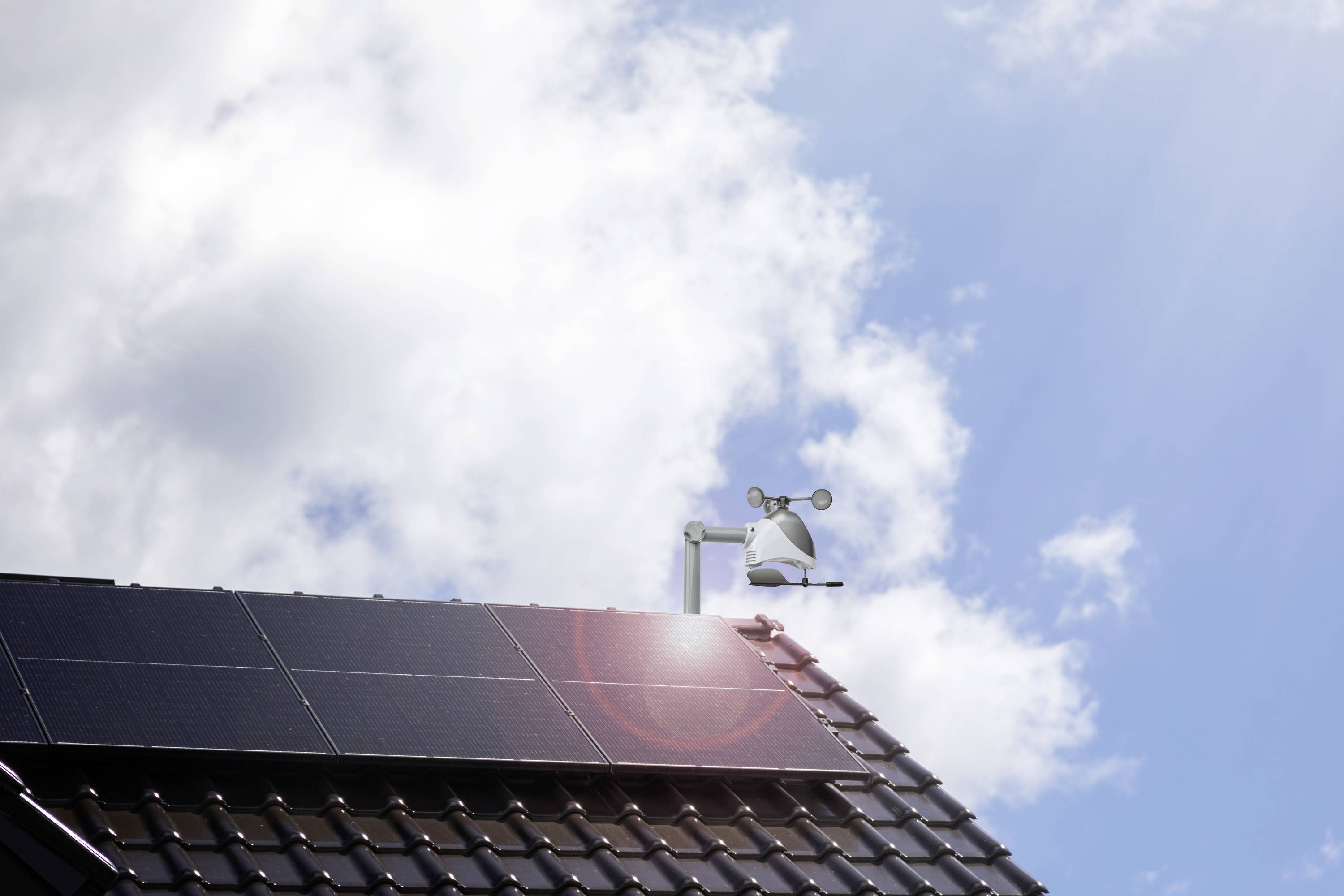 Solar roof with a clear sky in the background. Solar panels on a pitched roof, with a weather station and wind gauge beside it.