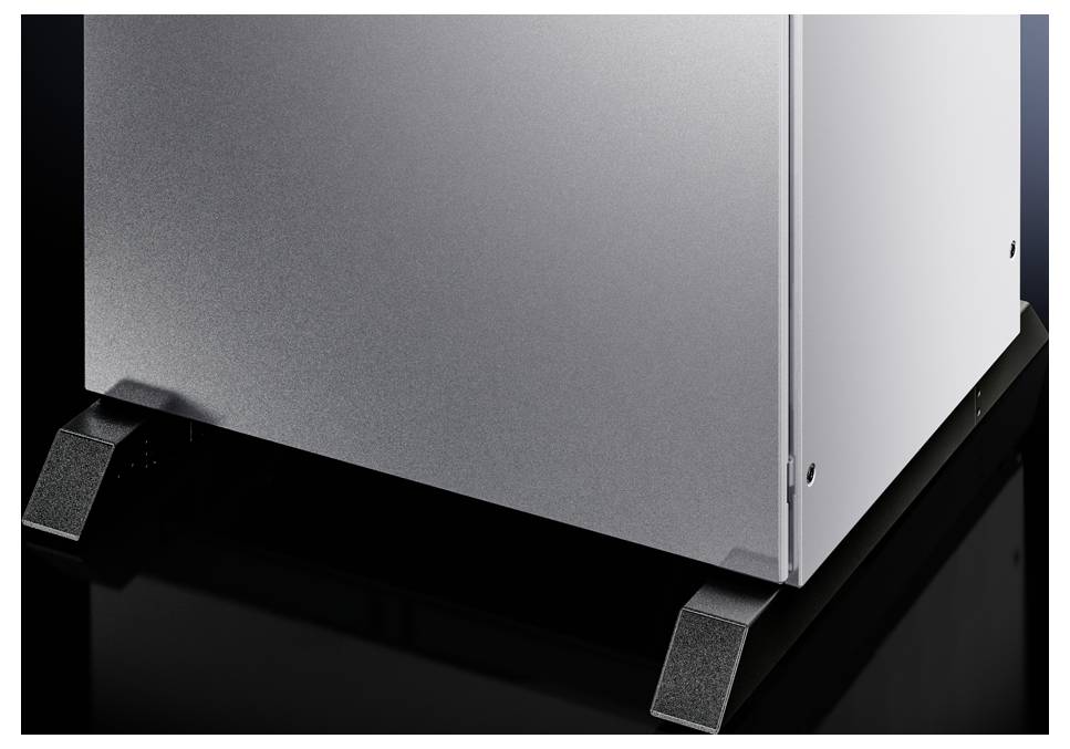 A metallic device housing stands on a glossy black floor. Only the lower part is visible, with stabilising feet.