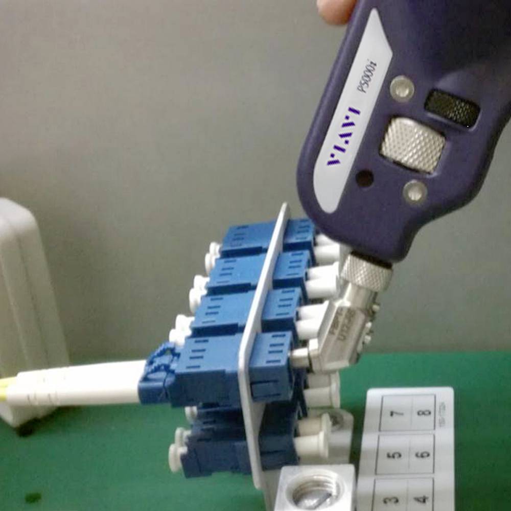 A purple handheld device is connected to a blue technical device, which is placed on a green table. Technical analysis.