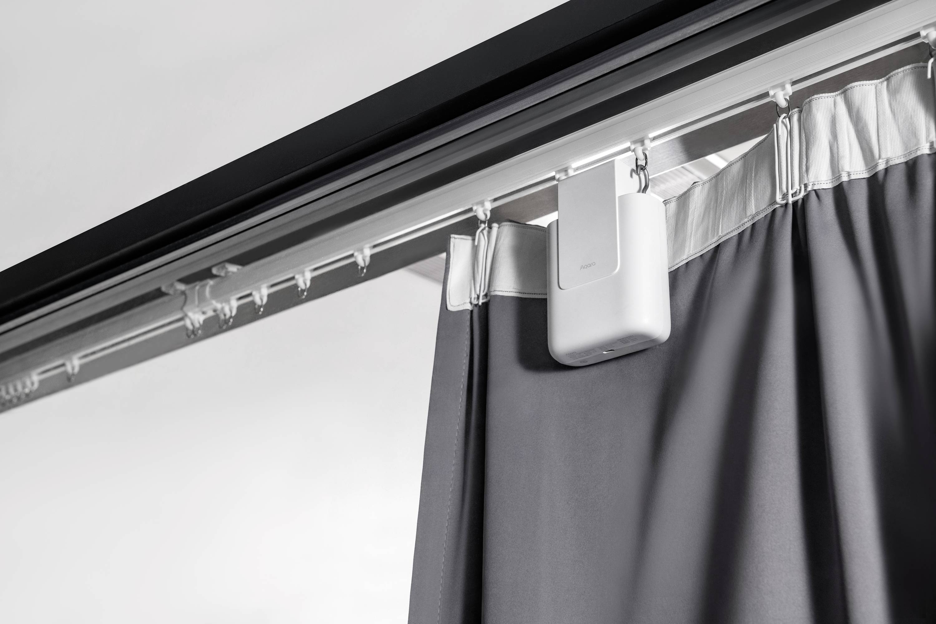 A grey curtain hangs from a track system, equipped with a small white motor for automatic operation.