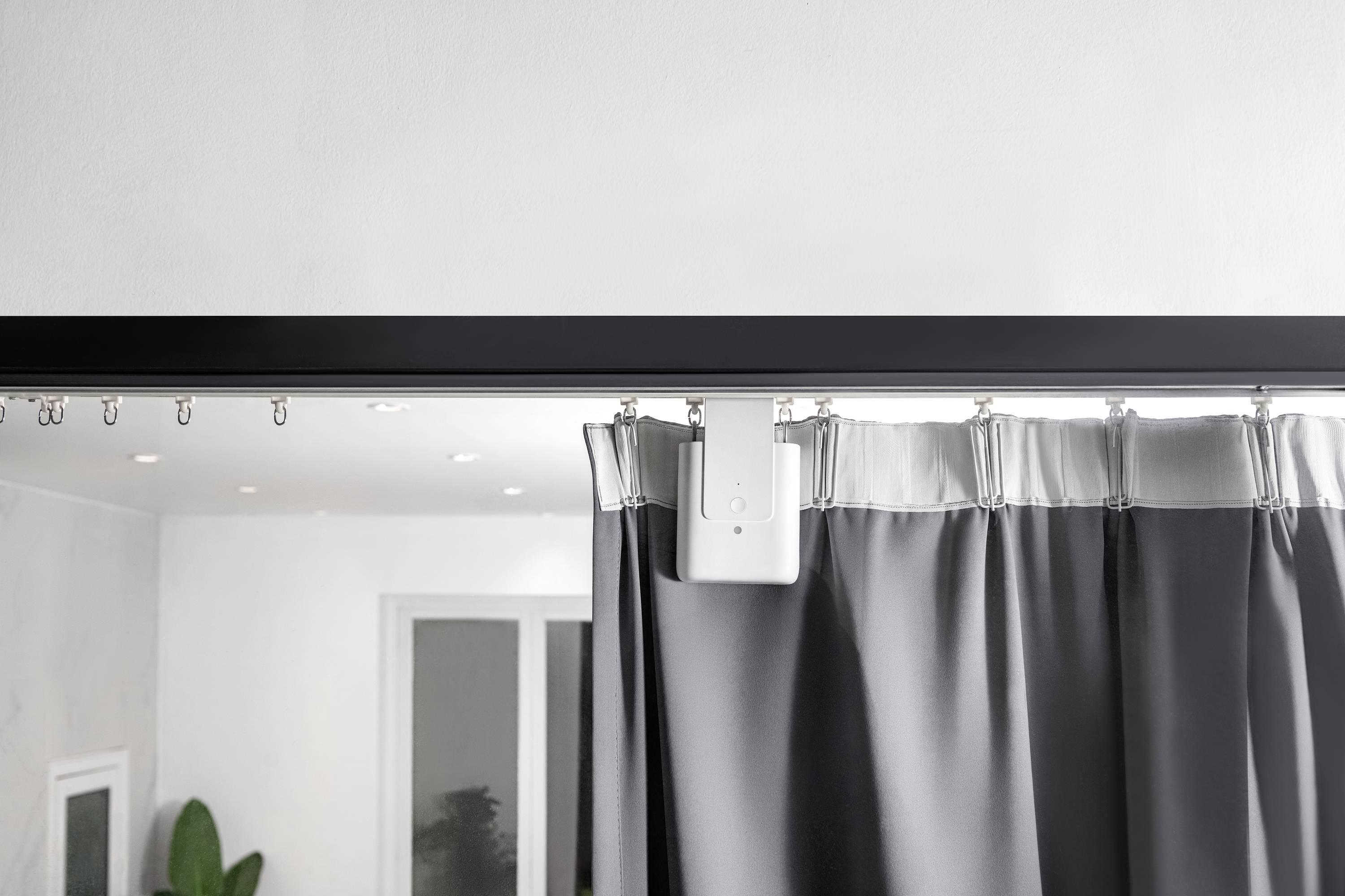 A curtain with an automatic sliding system, suspended from a black curtain pole, in a bright room with a mirror.