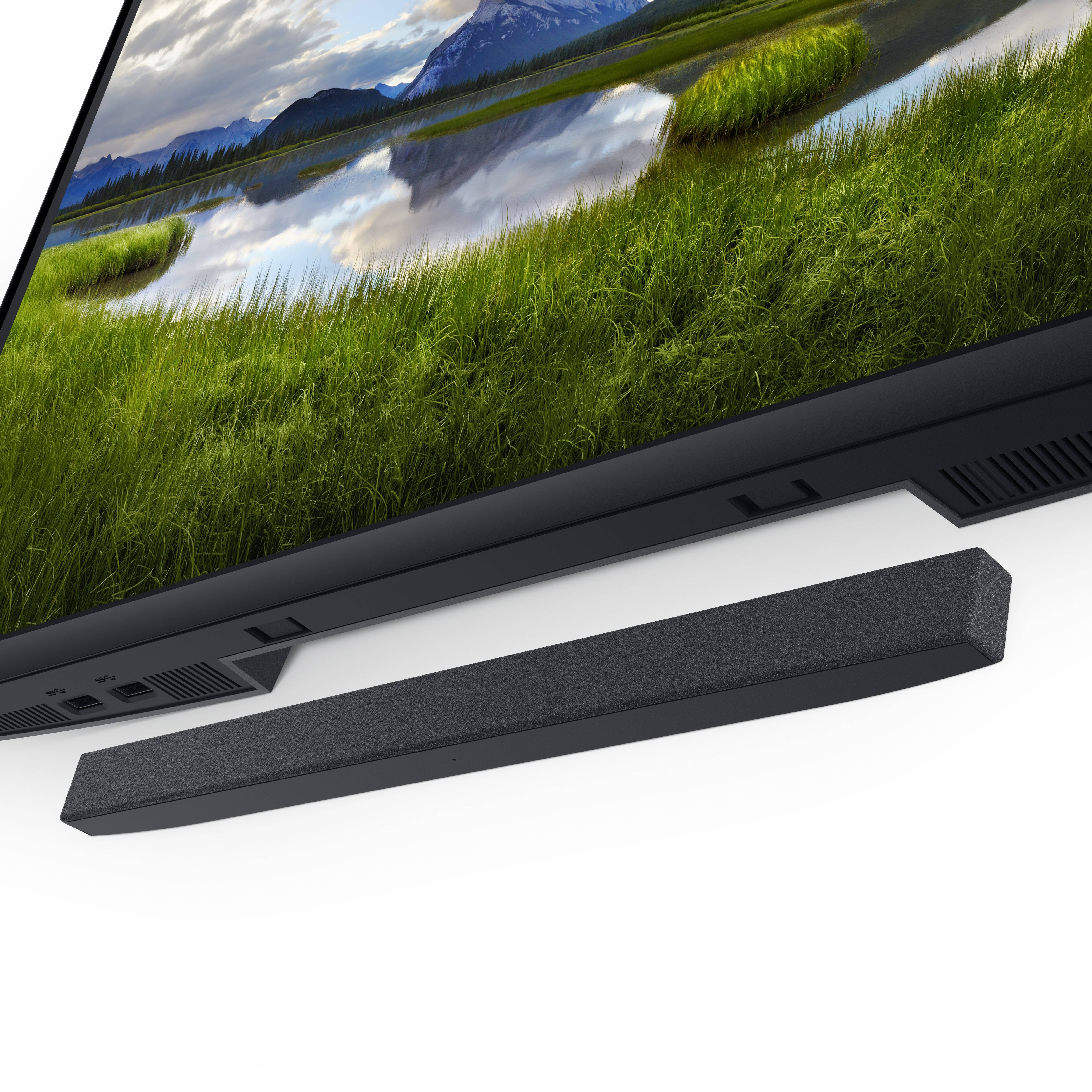 A laptop with a large screen displays a landscape of green meadows and mountains. Beneath it sits a black soundbar.