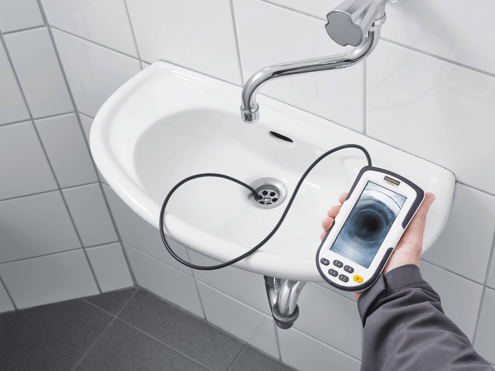A person is holding an inspection camera with an image of a blocked pipe over a sink.