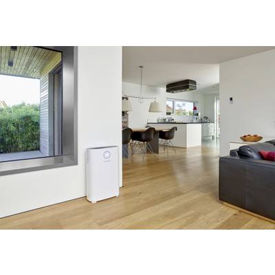 A modern living room with wooden flooring, a grey sofa, an air purifier against the white wall, and an open-plan kitchen in the background.