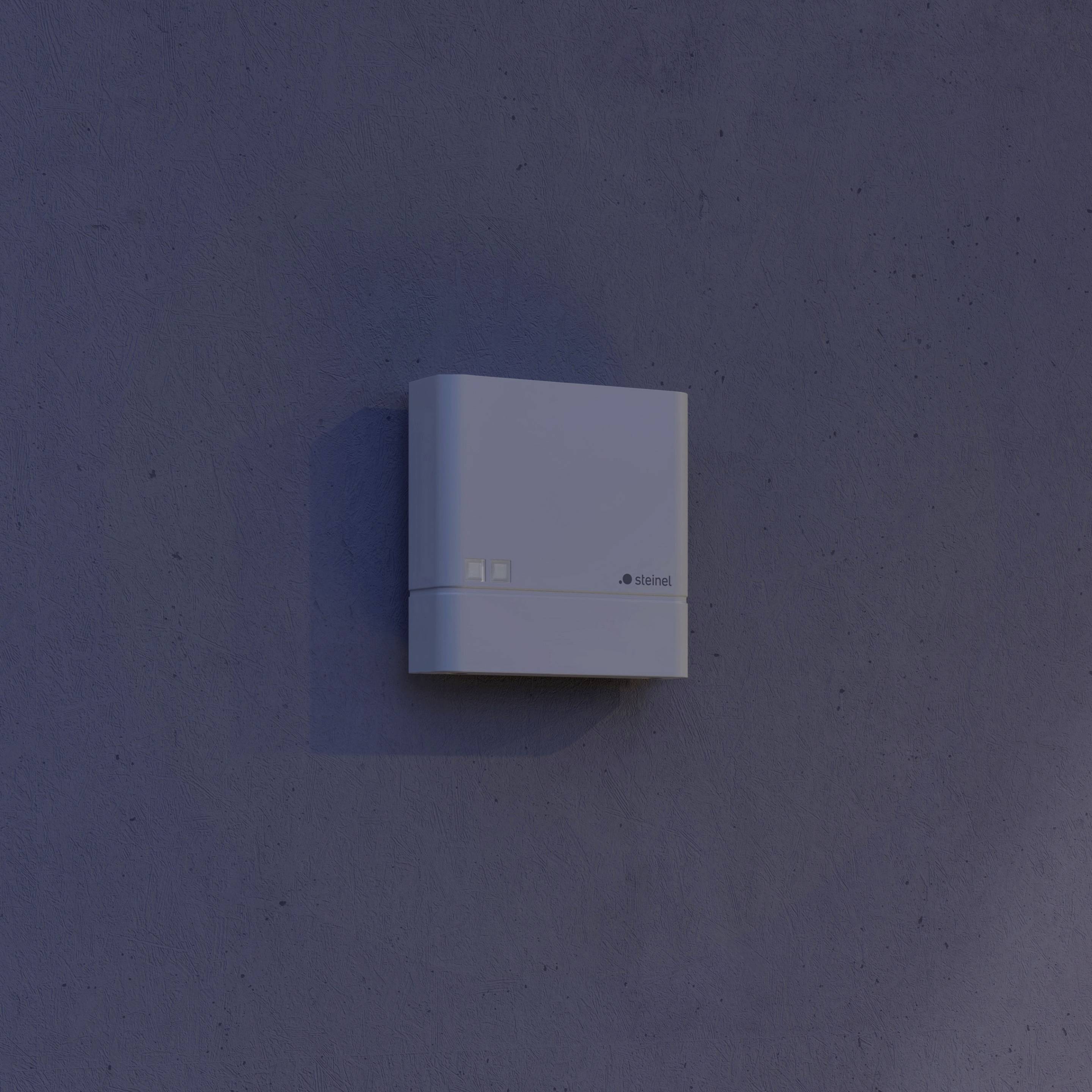 A white, square box of an electronic device is mounted on a blue-grey wall. The device has a minimalist design.