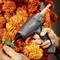 A hand holds a hot glue gun over orange marigolds, ready for crafting or mounting.