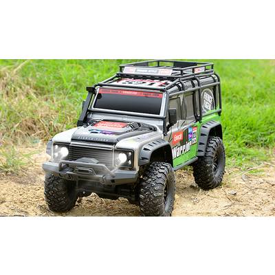 A model off-road vehicle drives over sandy earth and grass. It has large tyres and sporty stickers.