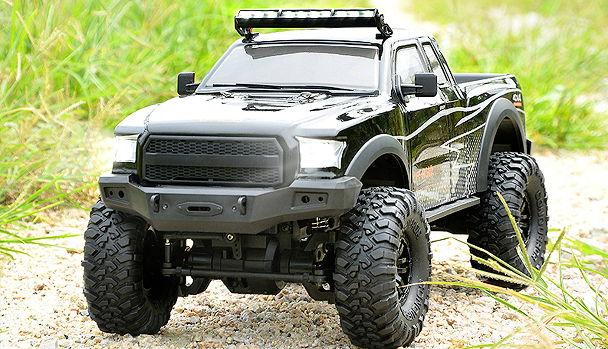 Remote-controlled black off-road model car with chunky tyres drives along a rocky path, surrounded by grass.