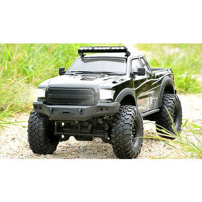 Remote-controlled black off-road model car with chunky tyres drives along a rocky path, surrounded by grass.