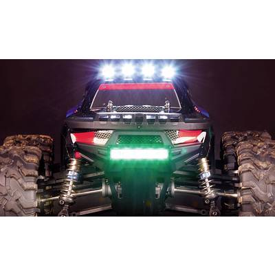A remote-controlled car in a close-up view from the front, with illuminated LED lights, large off-road tyres, and visible suspension.