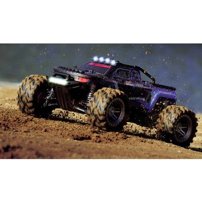 A remote-controlled car races across sandy ground at high speed. Dust and earth fly up behind its large tyres.