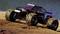 A remote-controlled car races across sandy ground at high speed. Dust and earth fly up behind its large tyres.