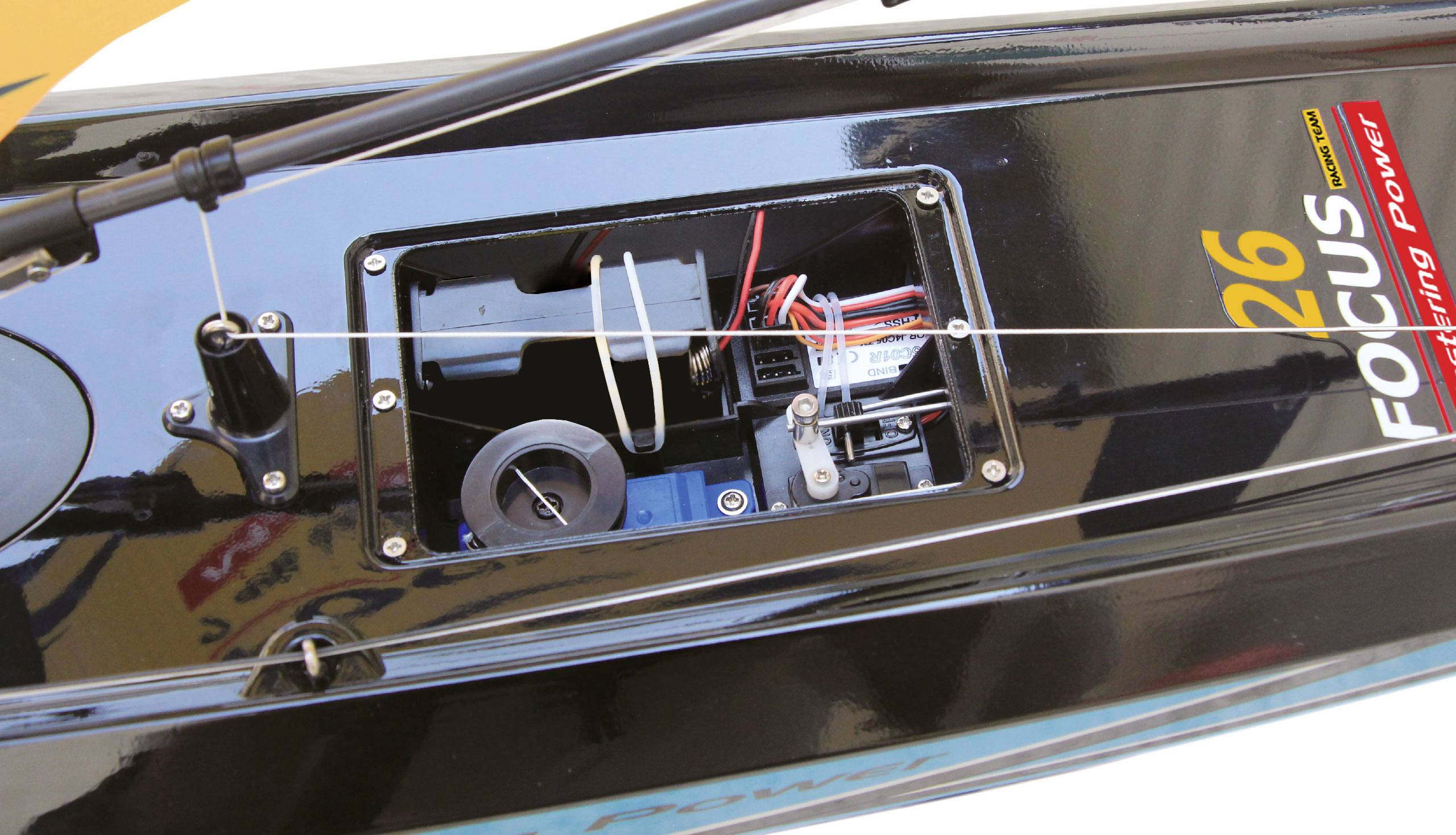 A remote-controlled model boat with an open compartment, revealing control electronics and wiring. Used for maintenance or repair.