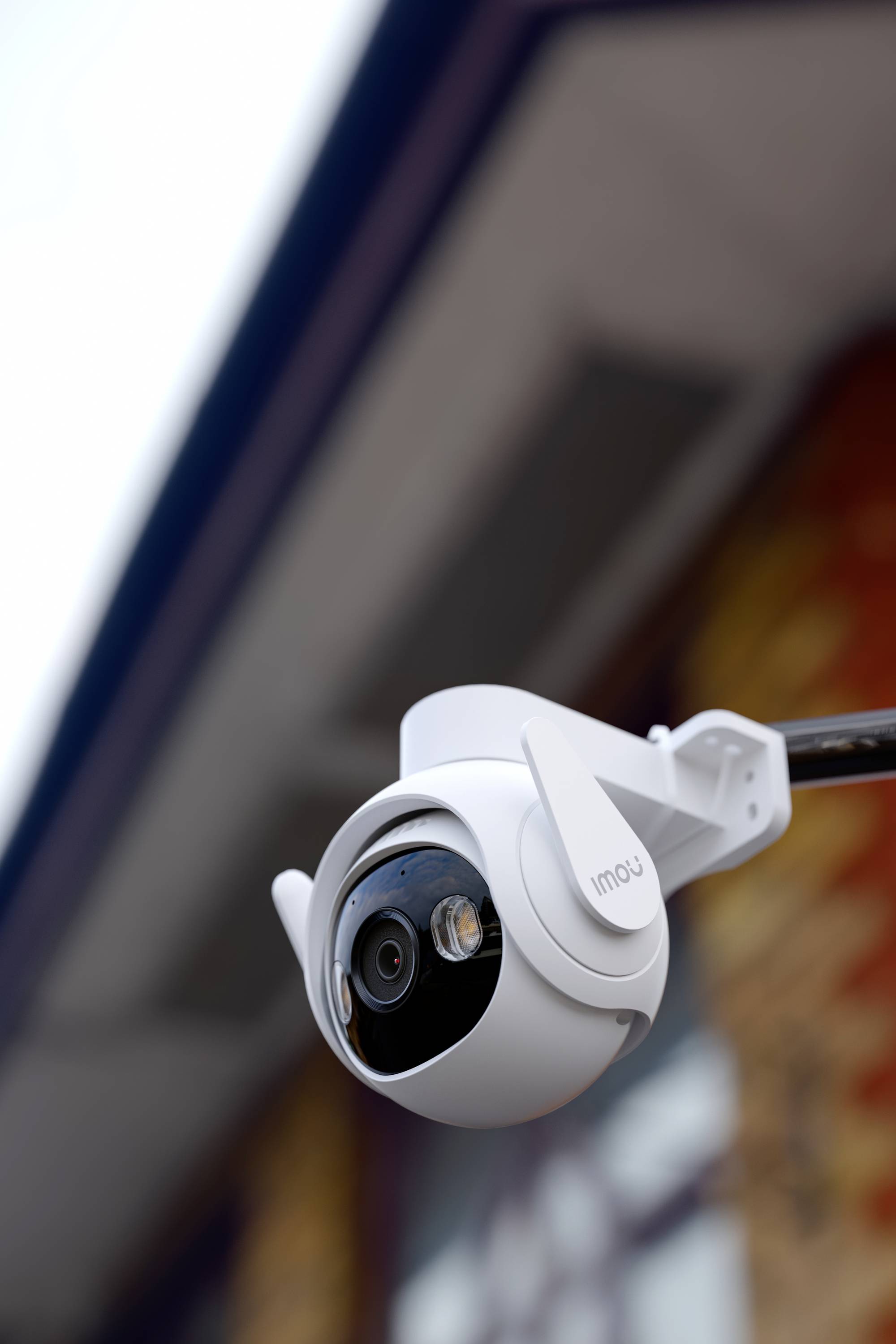 Security camera in close-up on a building wall, looking downwards. Surrounded by a blurred background.