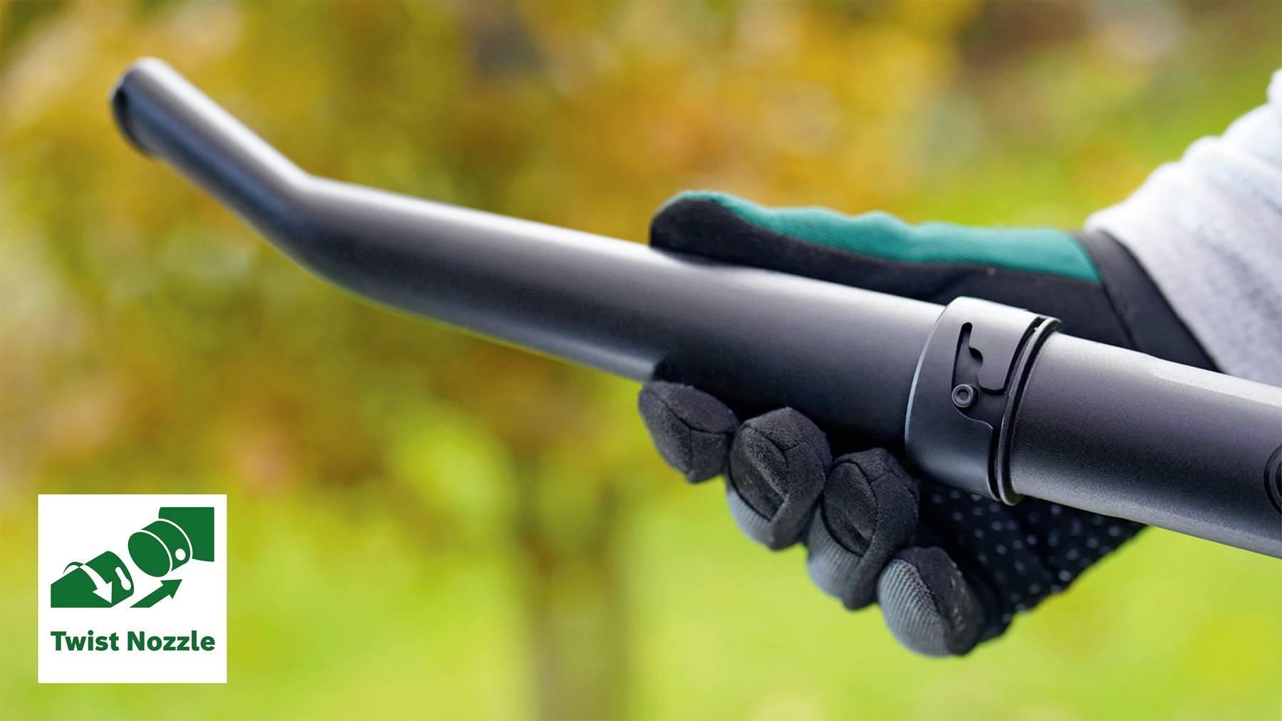 A gloved hand is holding a black pipe with a nozzle. Blurred autumn leaves are visible in the background. A 'Twist Nozzle' symbol indicates the twisting function.