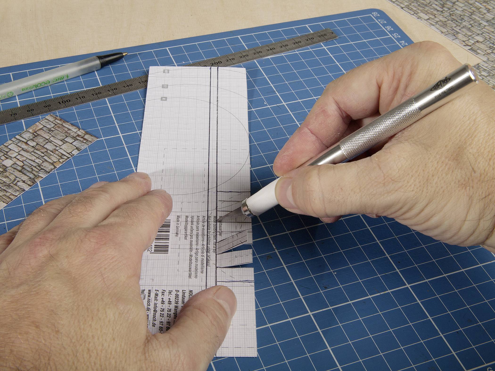 A person is cutting paper with a scalpel on a cutting board marked with a ruler.