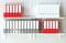 A shelf with lever arch files in red and white. Top row alternating between red and white folders, bottom row grey and red.