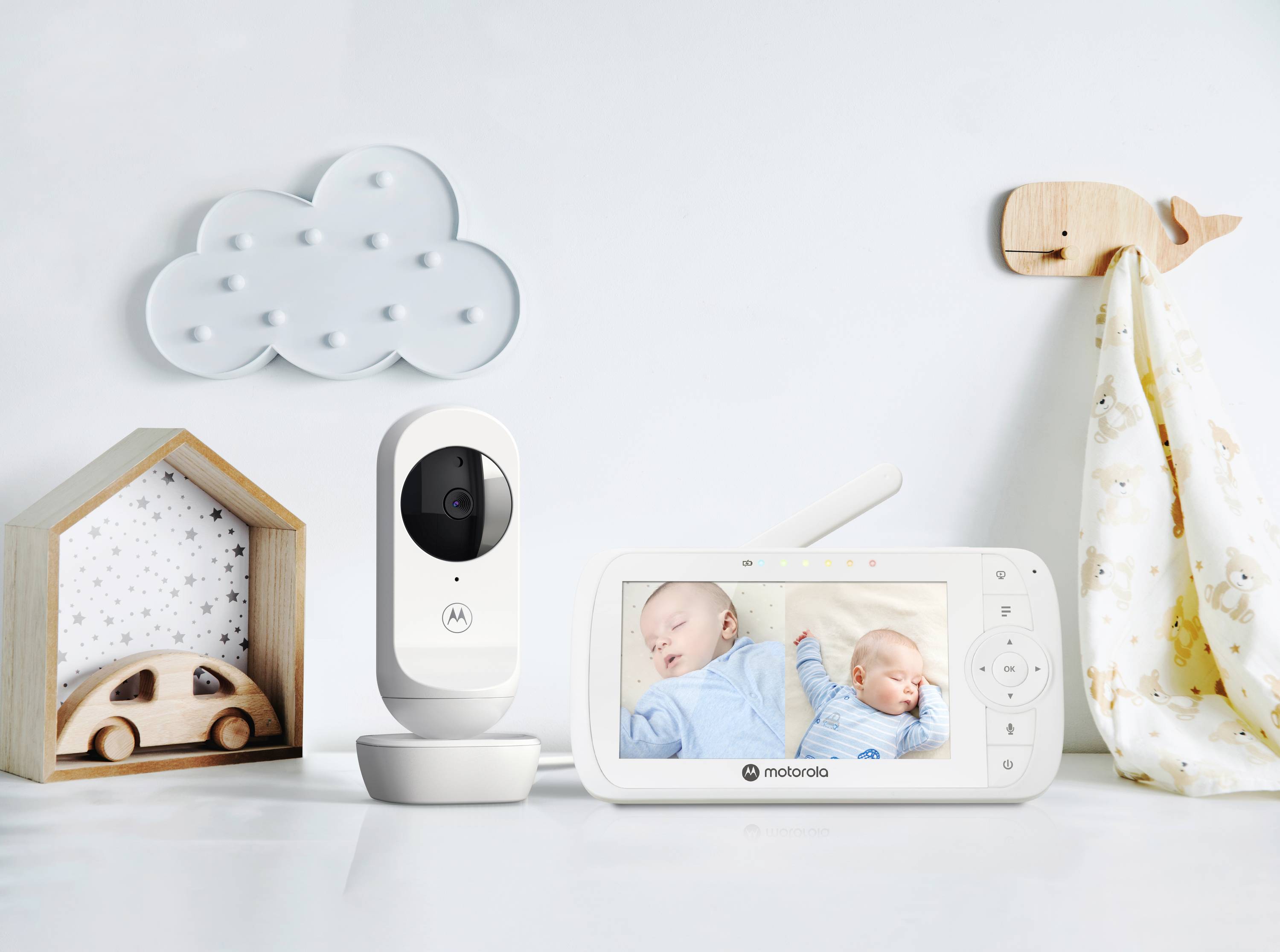 Baby monitor and camera showing sleeping babies. Camera set on white table with cloud and house decorations in the background.