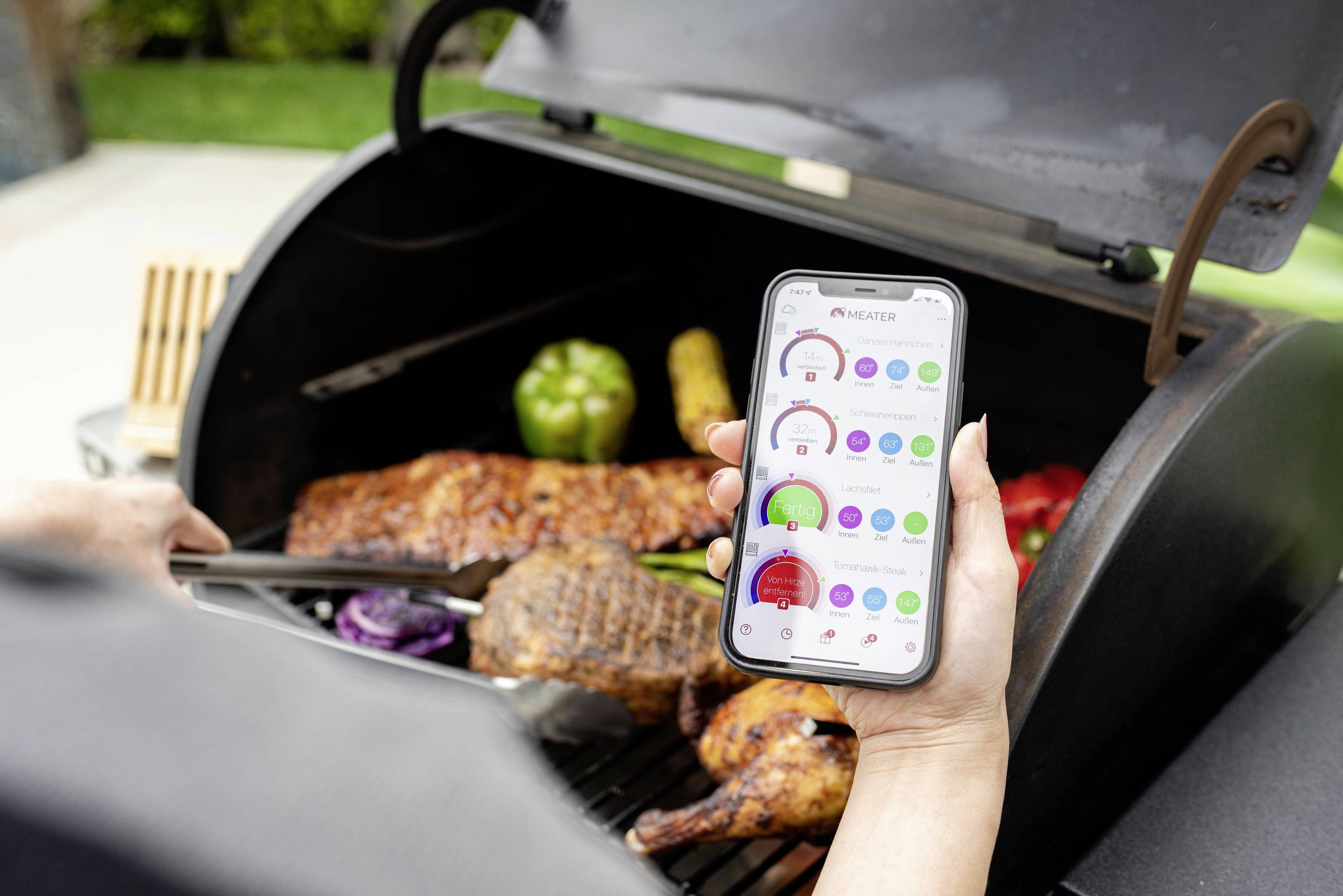 A person is grilling meat and vegetables and monitoring the temperatures using an app on their smartphone.