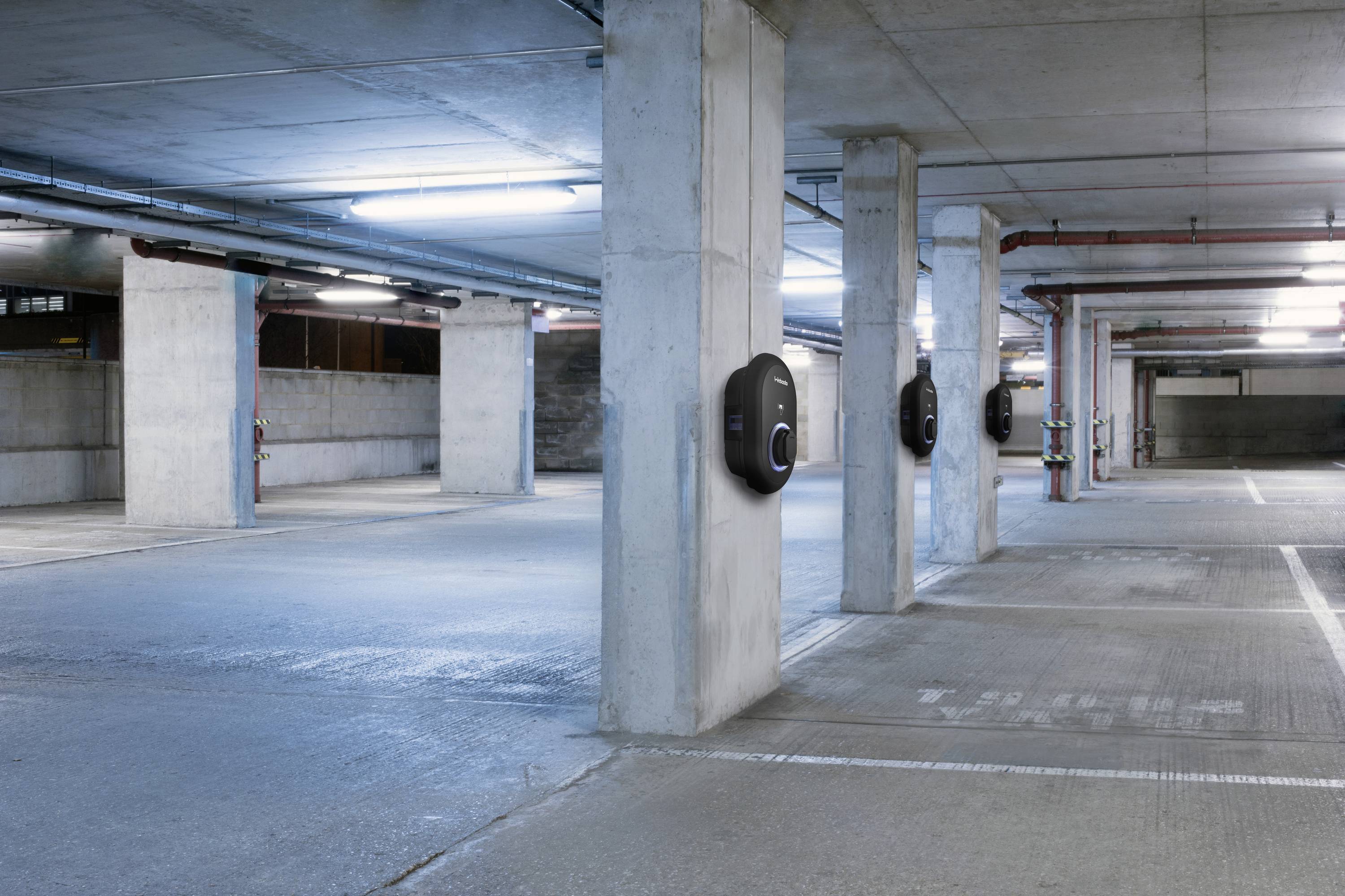 Empty underground car park with multiple charging stations for electric vehicles at the columns. Lighting provided by neon tubes on the ceiling.