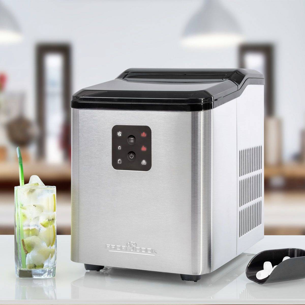A silver ice maker sits on a kitchen worktop next to a glass filled with ice cubes and a small scoop.