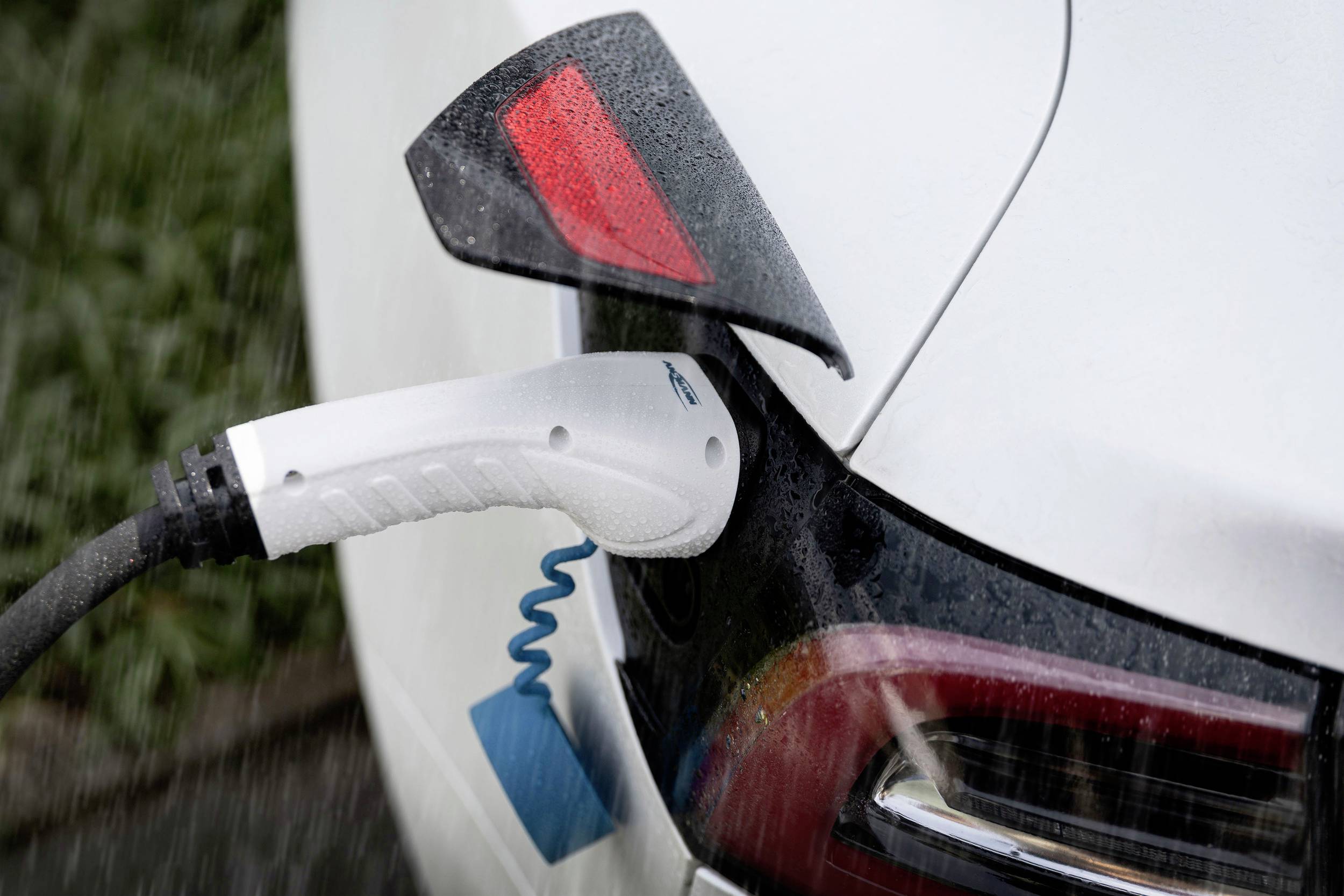 Electric car charging at a charging station in the rain. Close-up shows the charging cable plugged into the vehicle's charging port.