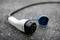 An electric vehicle charging plug lies in the rain on wet asphalt, its plug contacts protected and unused.
