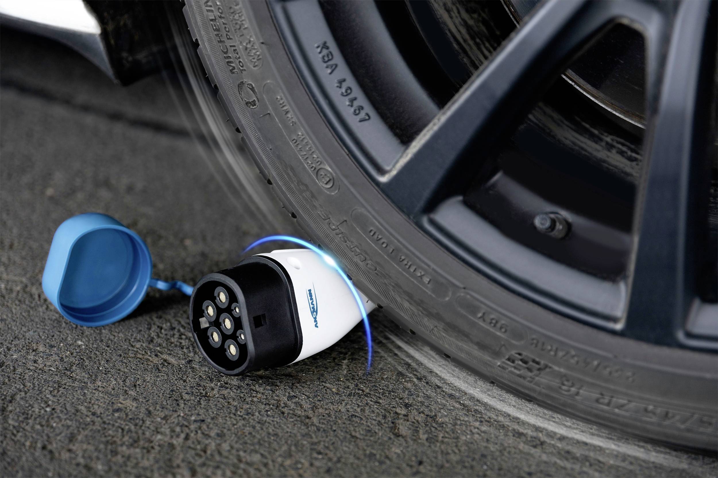Charging cable plug lies on the road next to a car tyre, ready for use.