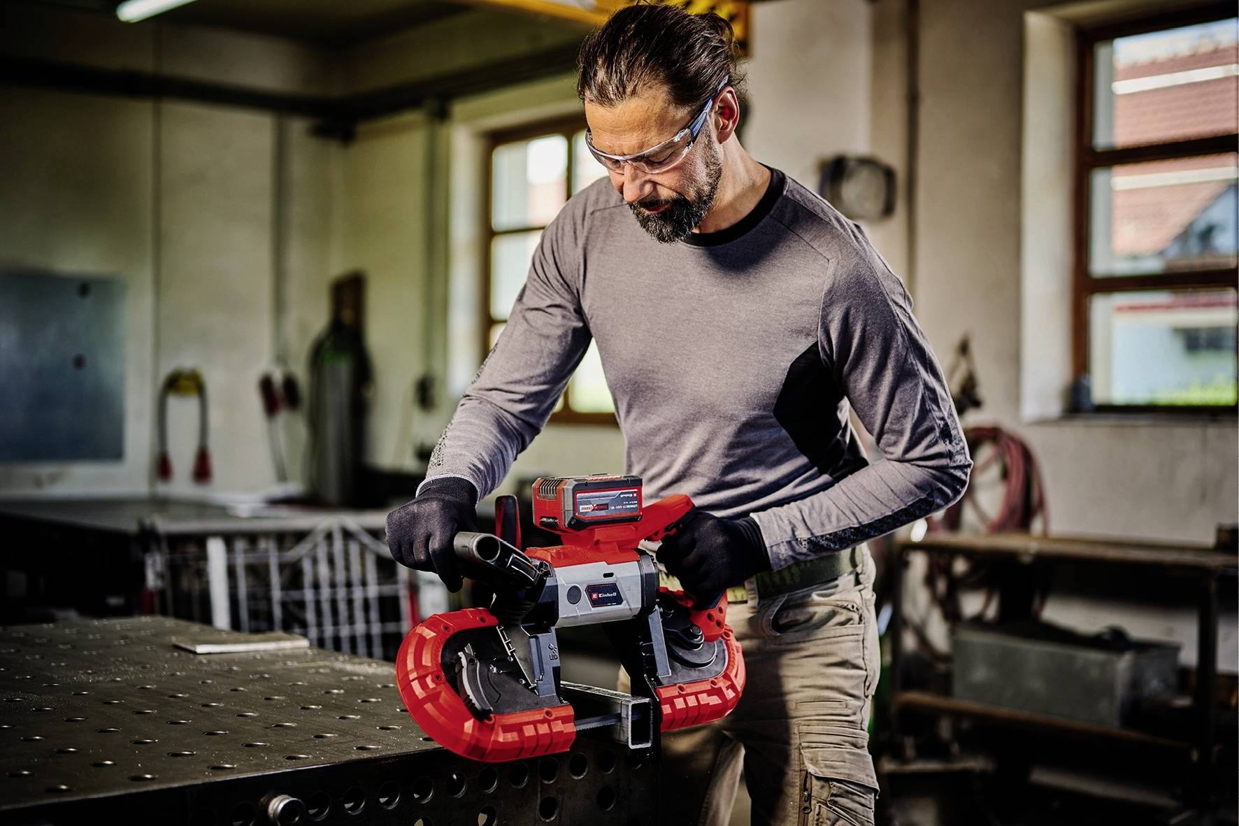 A man wearing safety glasses and gloves is working on an industrial-looking bandsaw in a workshop.