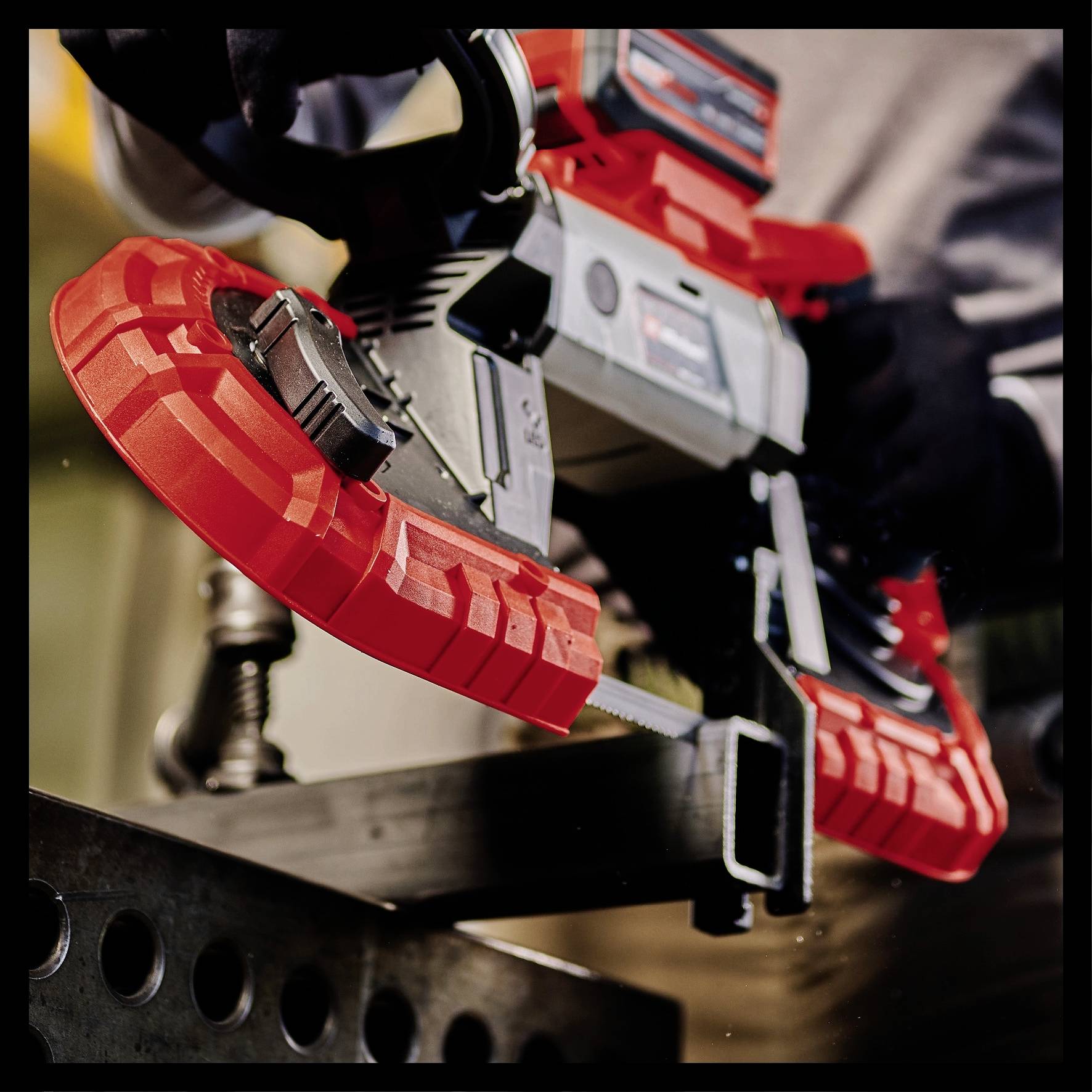 A person is using a red bandsaw to cut metal on a table. The scene depicts controlled work with protective equipment.