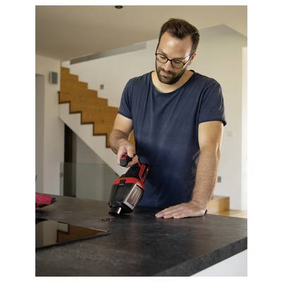 Man using a cordless vacuum to clean a kitchen countertop in a modern home, leaning over the counter near a staircase.<br>