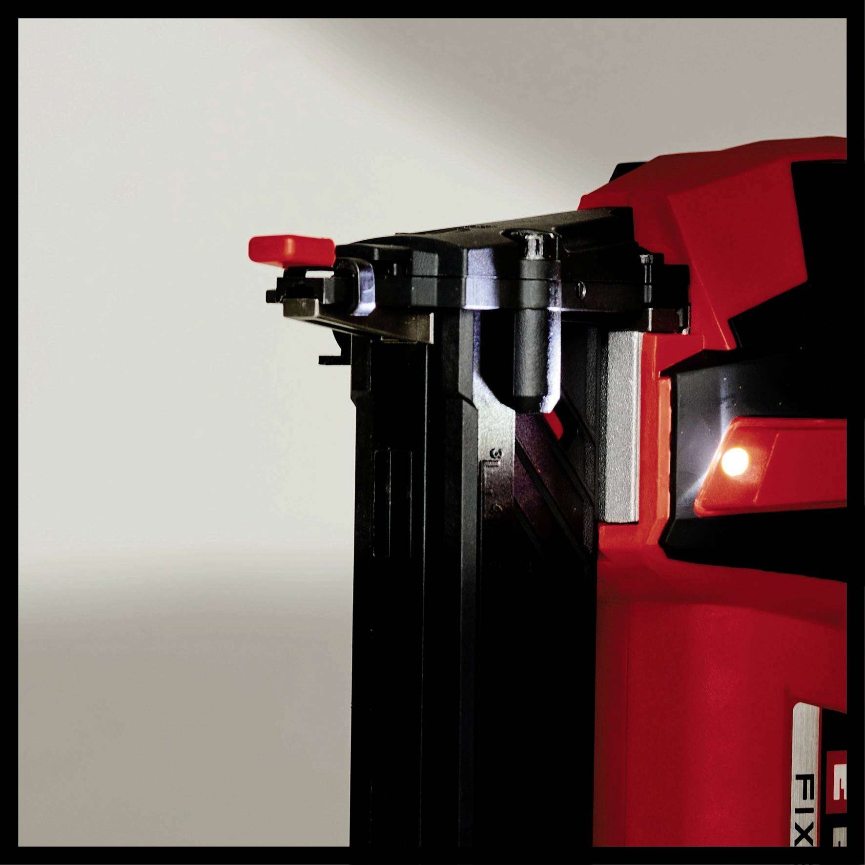 A red electric tool, possibly a nail gun or drill, shows a black tip with a red switch in the foreground.