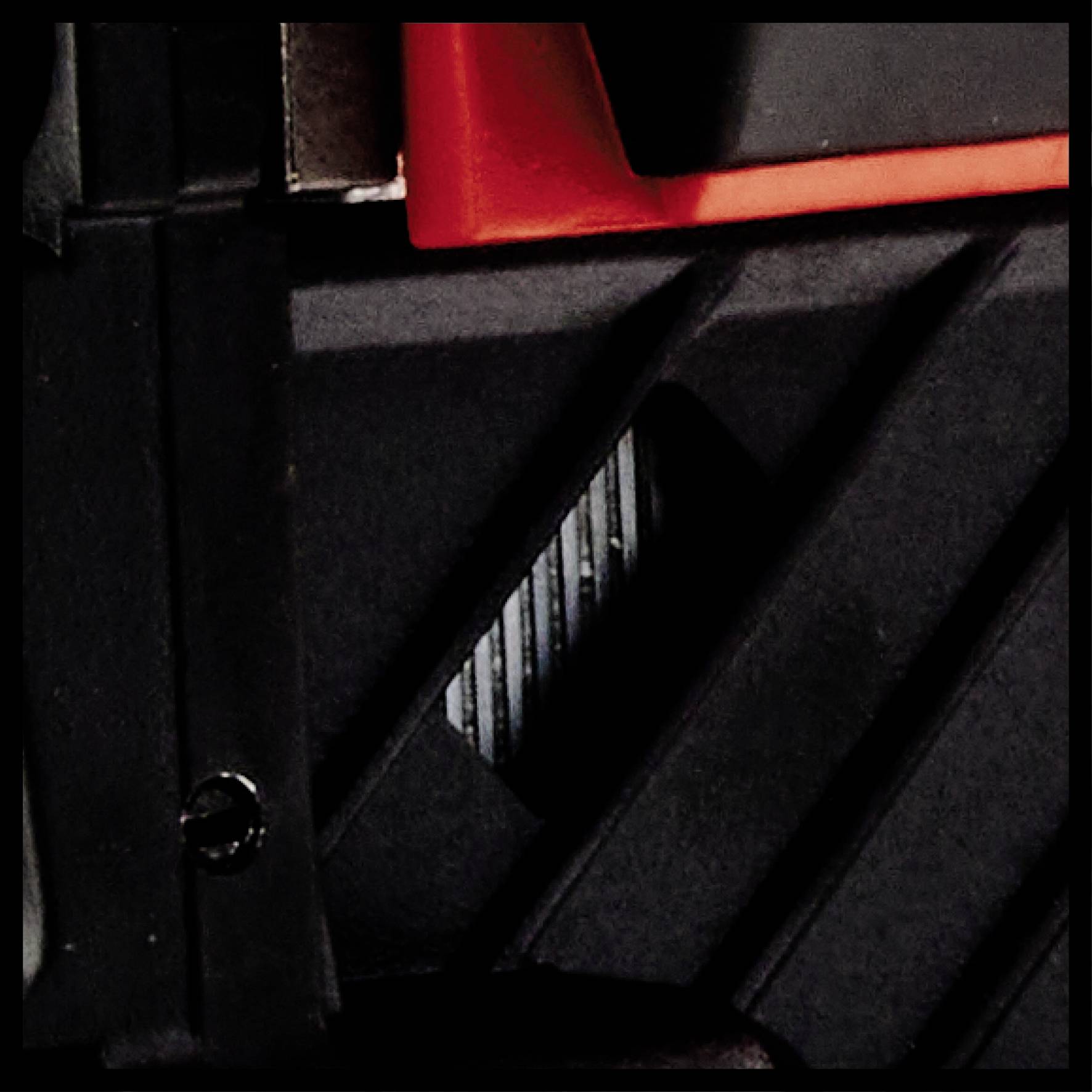 Close-up of a stylised mechanical object. Black and red elements, potentially part of a larger device or tool.