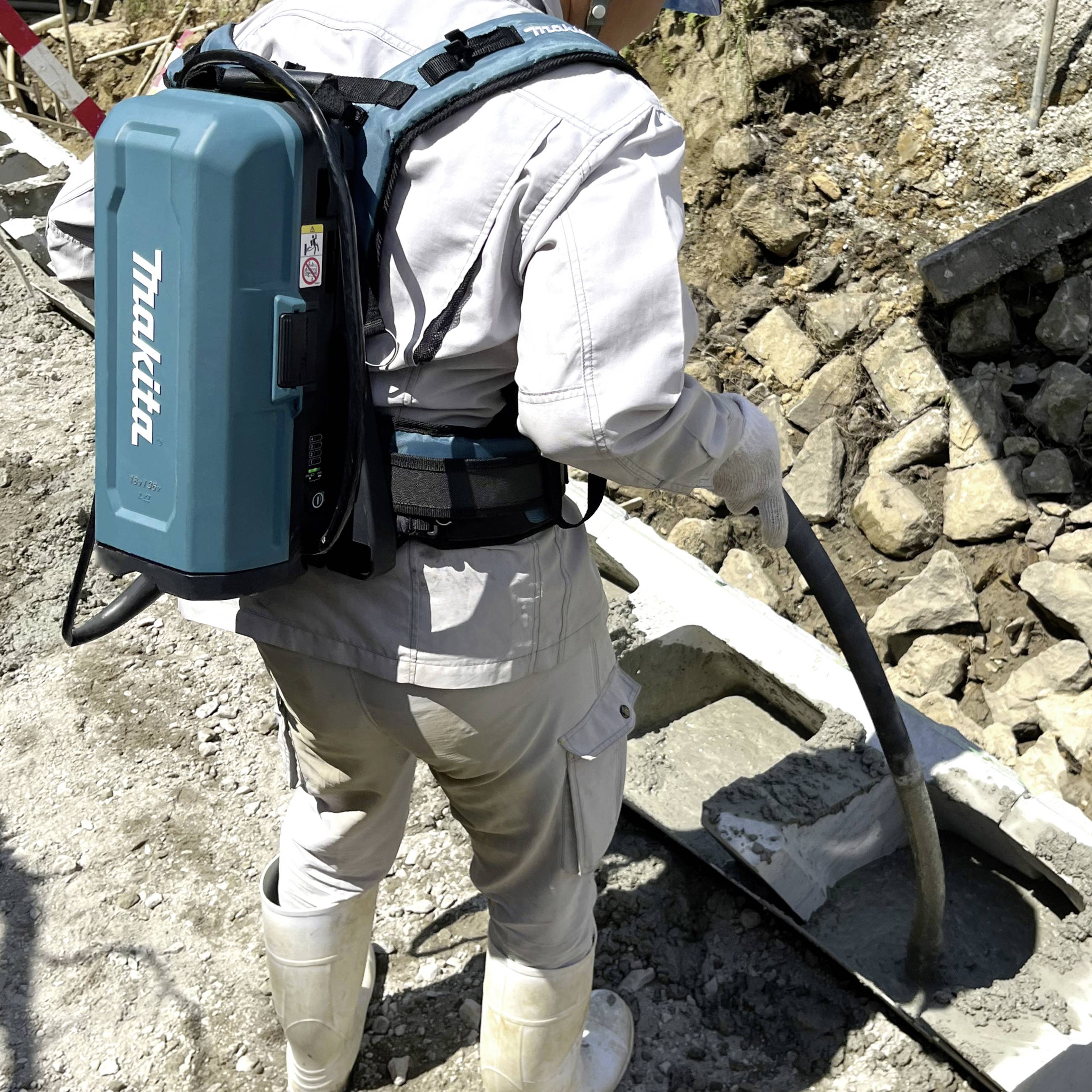 A person is using a portable concrete vibrator with a battery-powered device to compact fresh concrete into a mould.