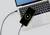 A smartphone is resting on a laptop keyboard and is being charged via a cable, with the charging screen displaying a green circle with a lightning bolt symbol.