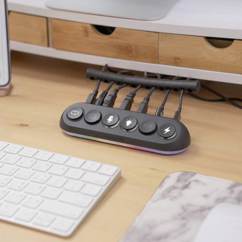 Several cables are connected to a simple, black docking station with symbols. It is situated on a desk.