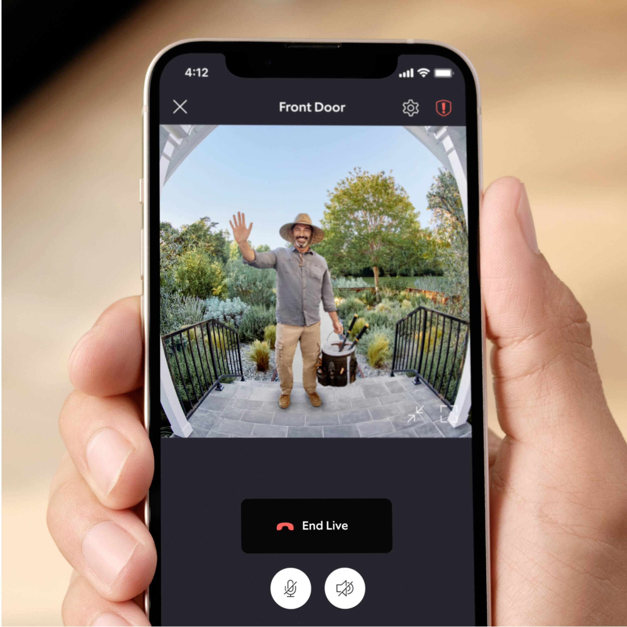 A person is standing outside on a veranda, waving at a surveillance camera visible on a smartphone screen.
