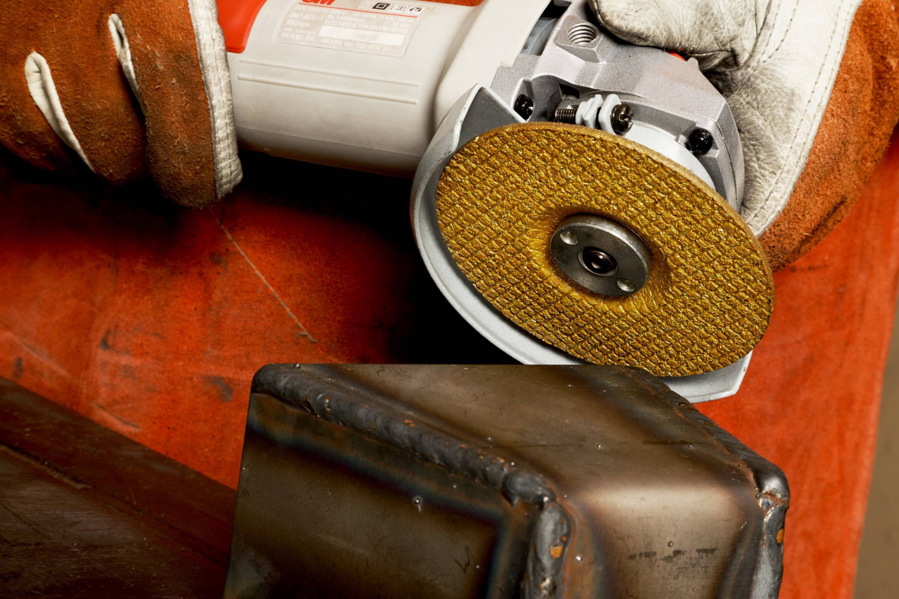 A person is grinding a metal construction using an angle grinder. The person is wearing protective gloves.