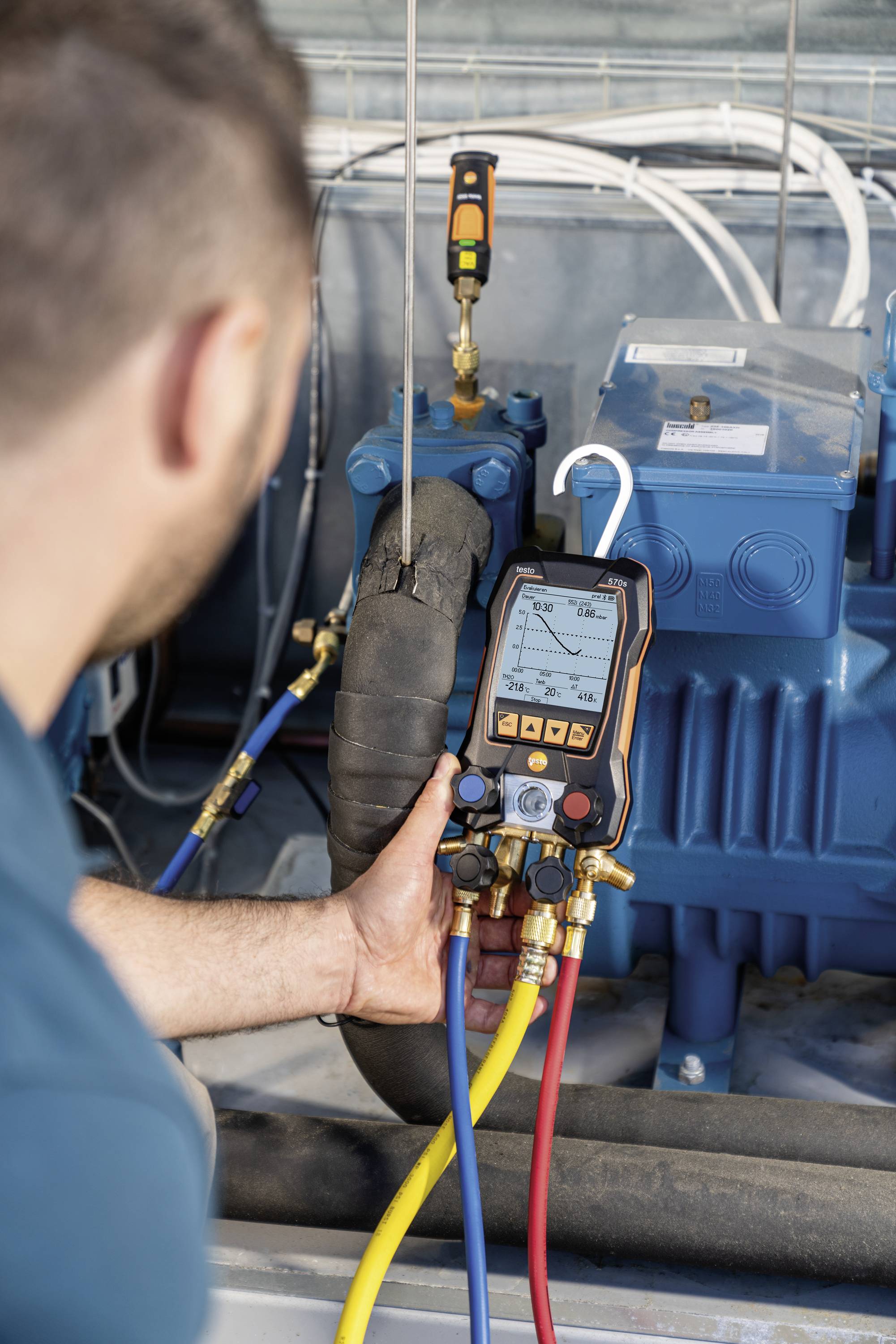 A technician is checking the pressure readings with a digital manometer on a blue machine with coloured hoses in the foreground.